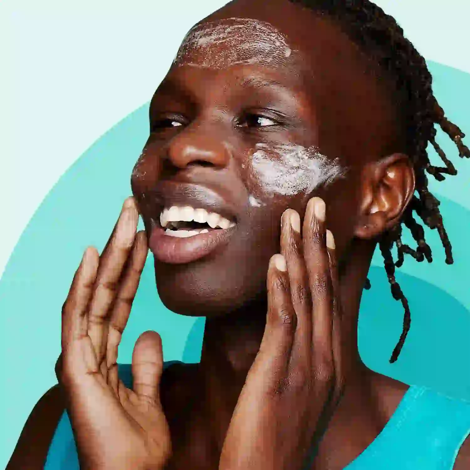 A person, smiling and applying face cream with both hands, stands against a turquoise background, exuding a sense of freshness and skincare routine.