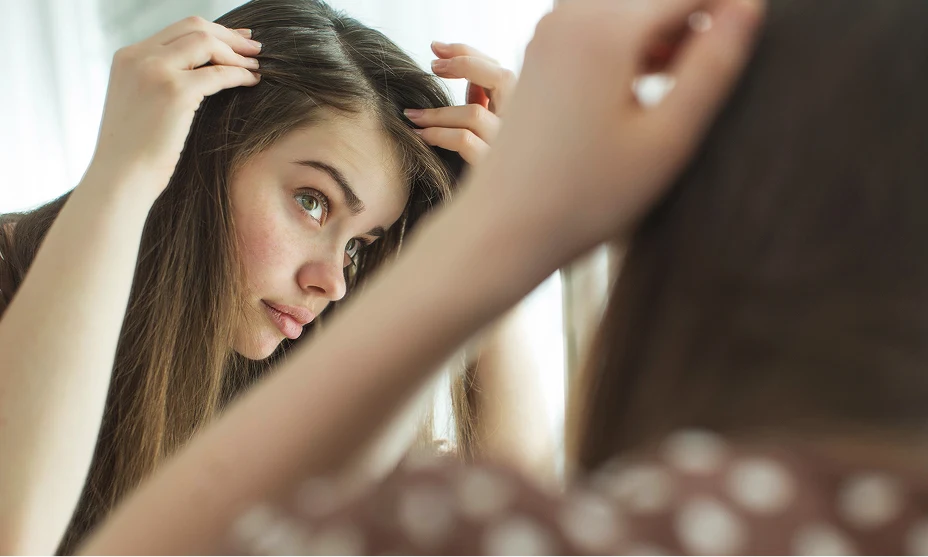Woman with long, light brown hair checking her part in the mirror