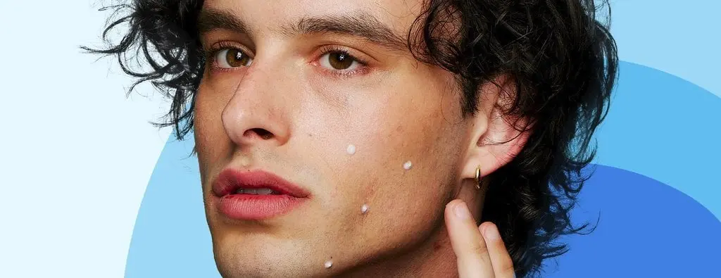 A person with curly hair is applying small white dots on their cheek. The earlobe has a gold hoop earring. The background features blue gradient curves.