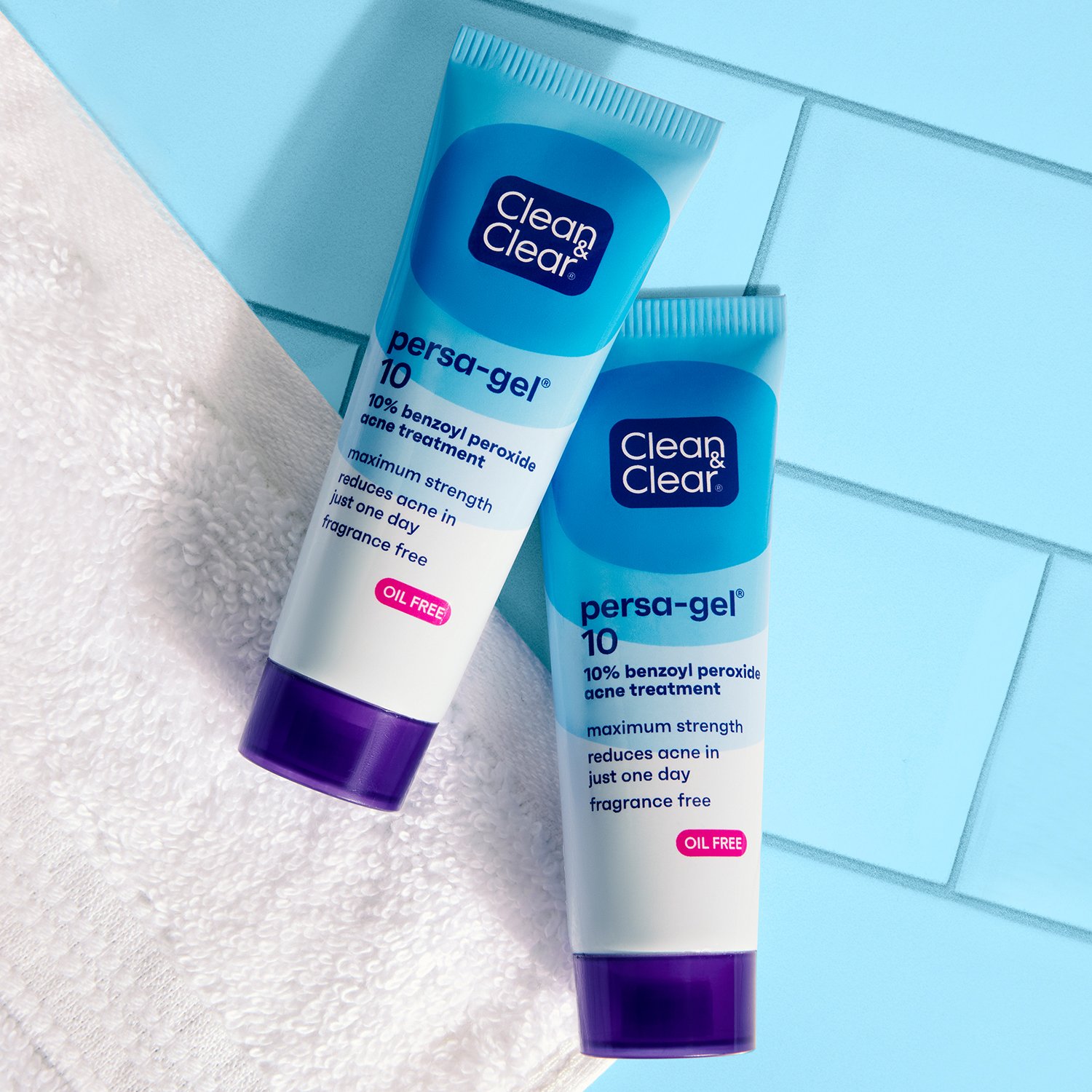 Two Clean & Clear Persa-Gel® 10 Acne Treatment Gel tubes positioned on a floor next to a textured floor cloth, showcasing the product's packaging and design.