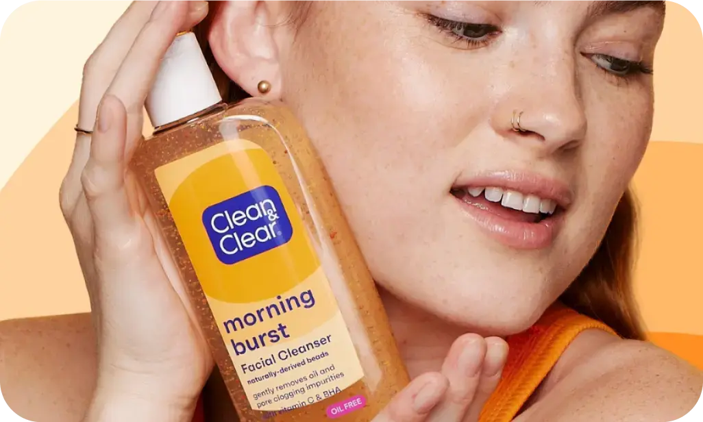 Clean & Clear skincare products featuring Vitamin C enriched Morning Burst Facial Cleanser held by a smiling woman.