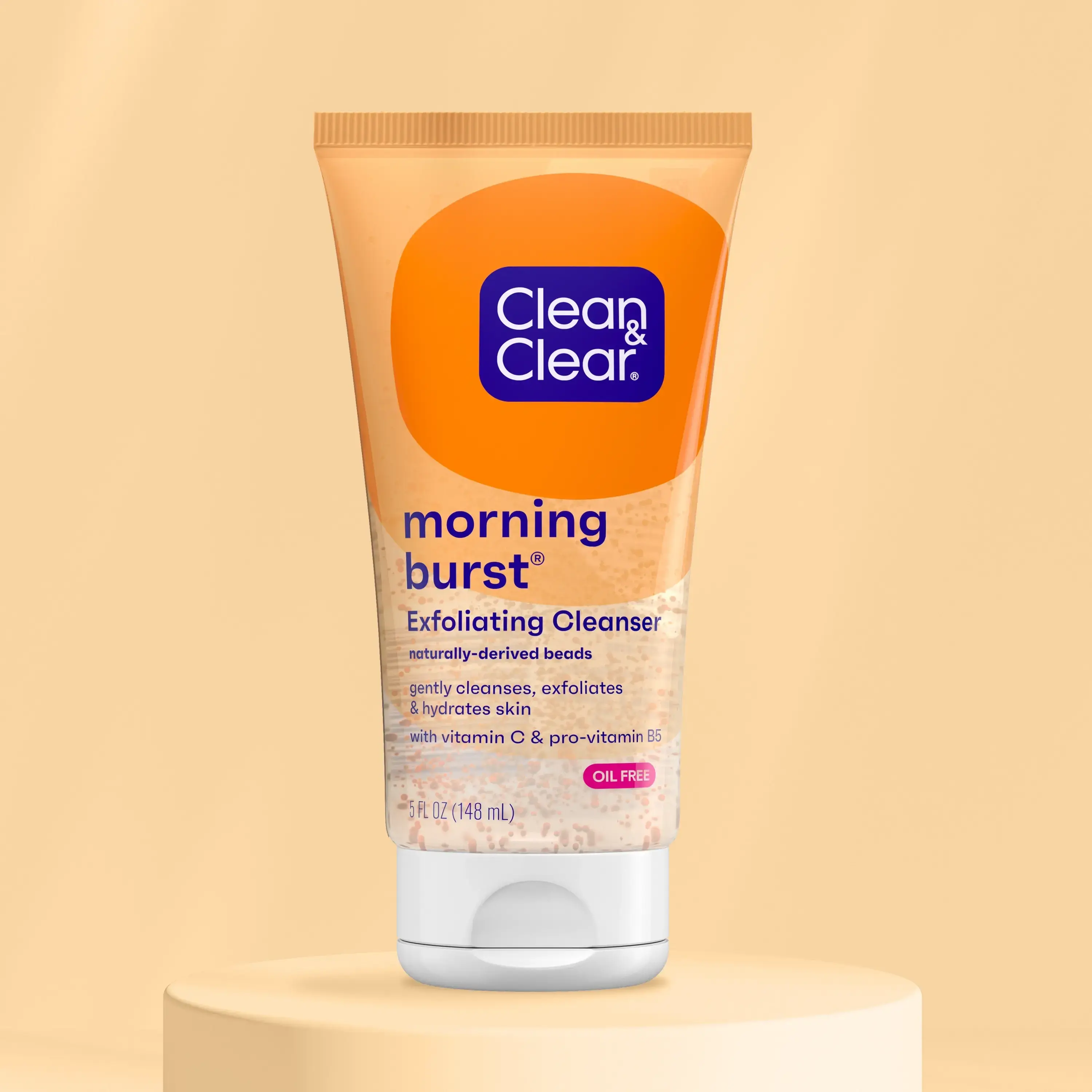 Tube of Clean & Clear morning burst exfoliating cleanser with naturally-derived beads sits on a round platform against a beige backdrop. Text: "gently cleanses, exfoliates & hydrates skin with vitamin C & pro-vitamin B5, OIL FREE, 5 FL OZ (148 mL)."