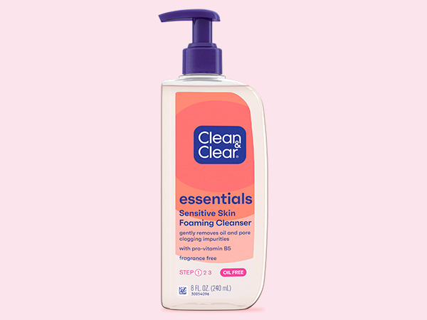 A pump bottle labeled "Clean & Clear essentials Sensitive Skin Foaming Cleanser" with pro-vitamin B5. The context is a pink background. It states "fragrance free, oil free, Step 2 of 3."