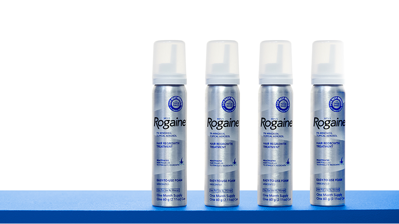 Four bottles of ROGAINE® Men's Topical Foam Four bottles of ROGAINE® Men's Topical Foam on a blue shelf with a white background