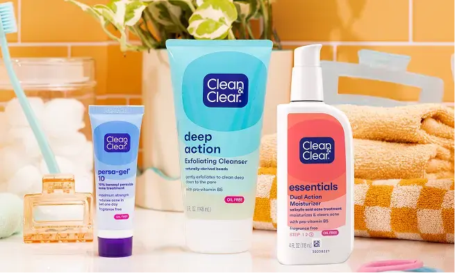 Clean&Clear® Persa-gel® 10 10% Benzoyl Peroxide Acne Treatment, Clean&Clear® Deep Action Exfoliating Cleanser and Clean&Clear® Essentials Dual Action Moisturizer on bathroom counter with towels, hair ties, plant and hairclips