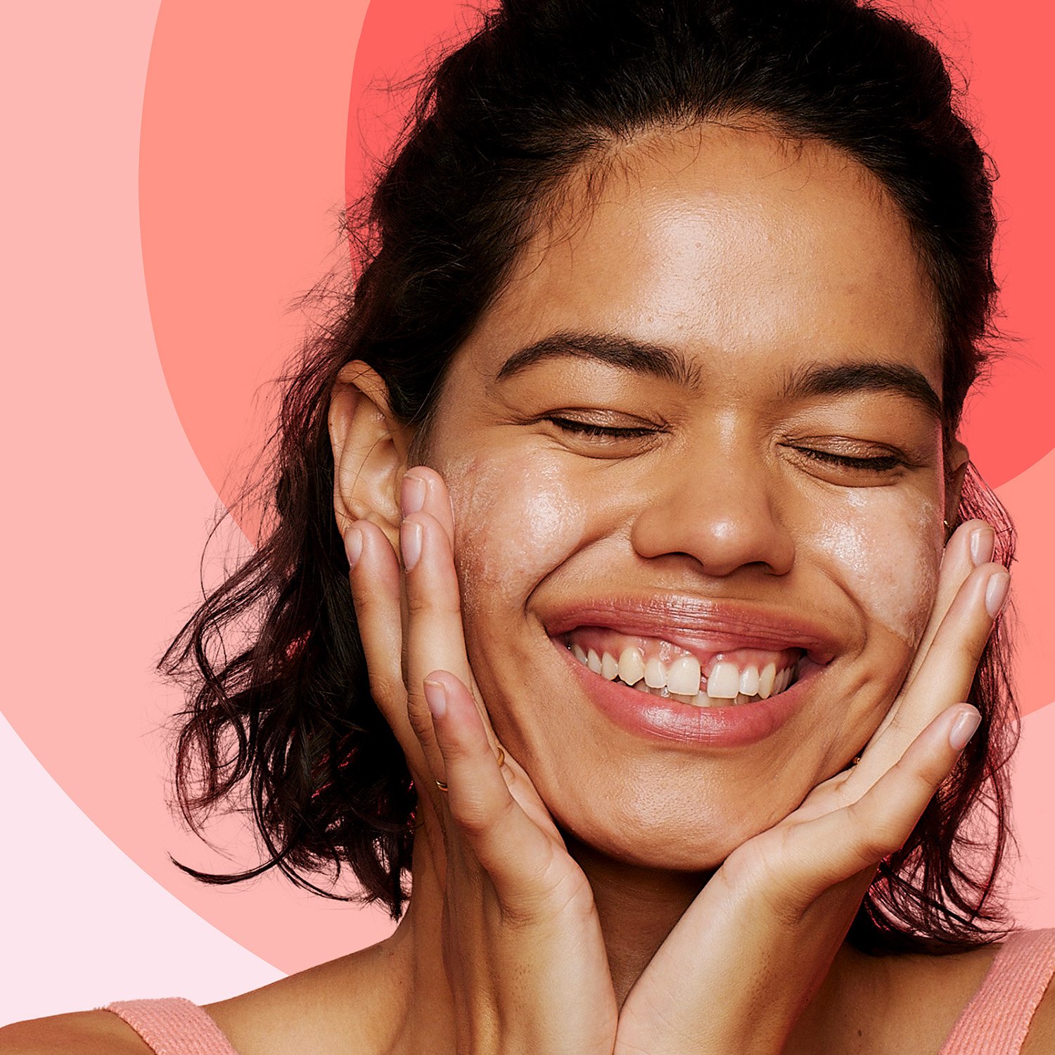 A smiling person gently touches their cheeks with both hands, eyes closed in enjoyment, against a pink and red gradient background.