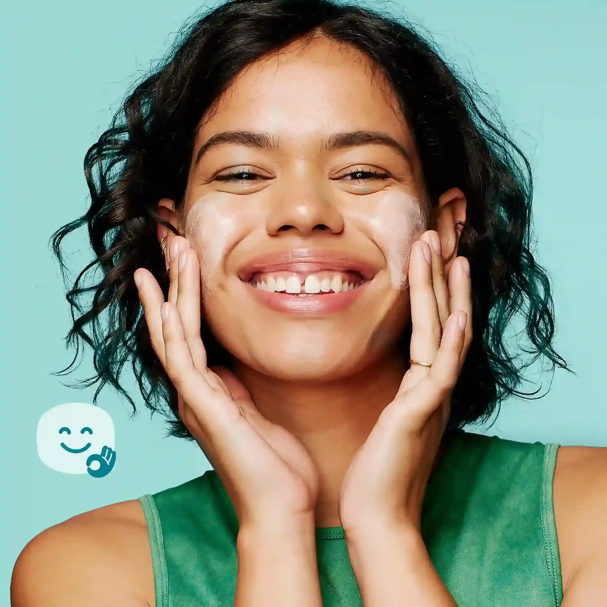 A smiling person with short black hair applies cream to their cheeks. A simple illustration of a smiling face and “OK” hand gesture is adjacent on a light teal background.