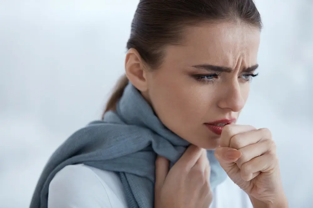 Brunette woman with a scarf around her neck, holding her throat in discomfort, showing signs of a sore throat.