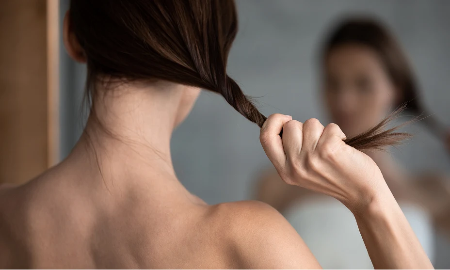  A woman with dark hair in a mirror reflection, holding a thinning section of hair