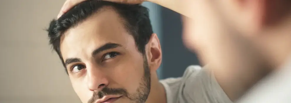Man with dark brown hair and beard checking his hairline in the mirror