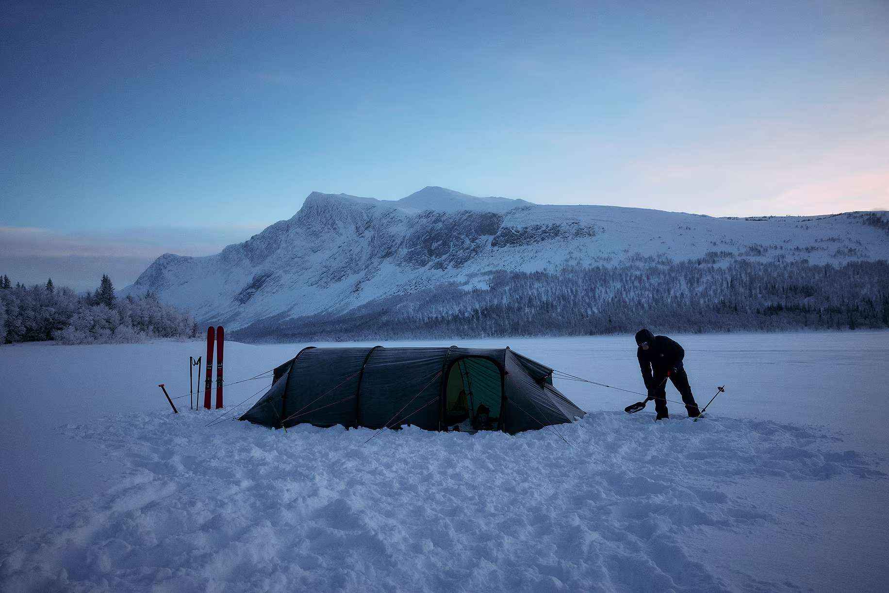 A man stands outside his tent in a snow-covered landscape.