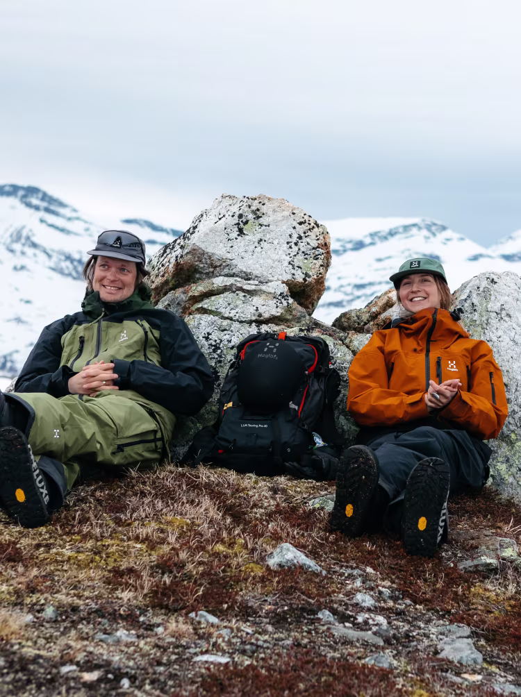 A man and a women sitting on a mountain in Haglöfs outdoor clothes