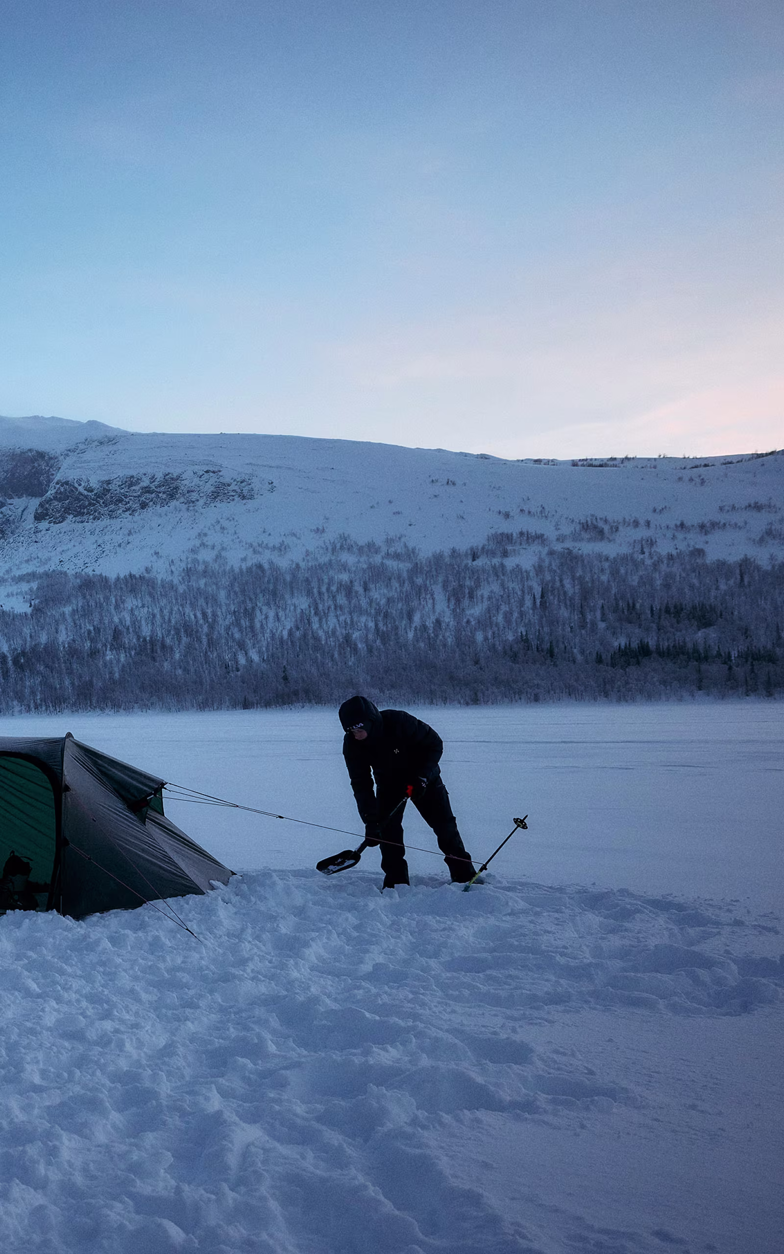 Shoveling snow to protect a tent  in the cold wearing a Haglöfs insulated jacket.