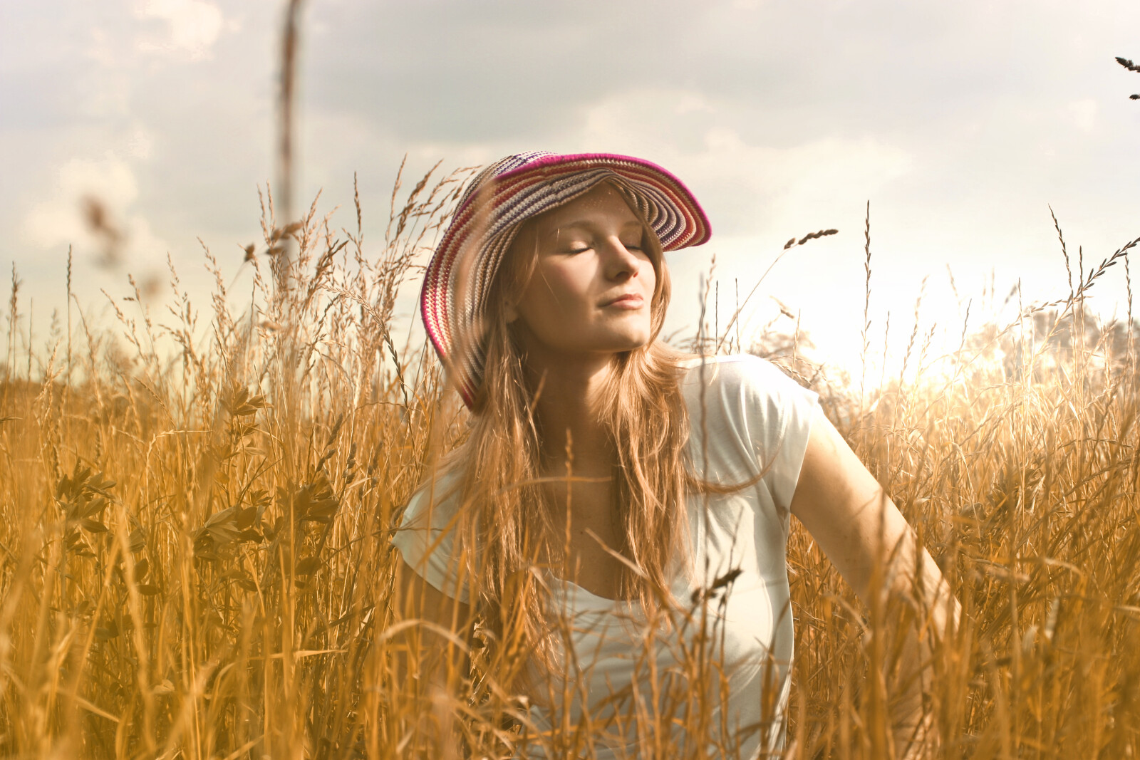 a woman in a field of wheat with a sun hat on 