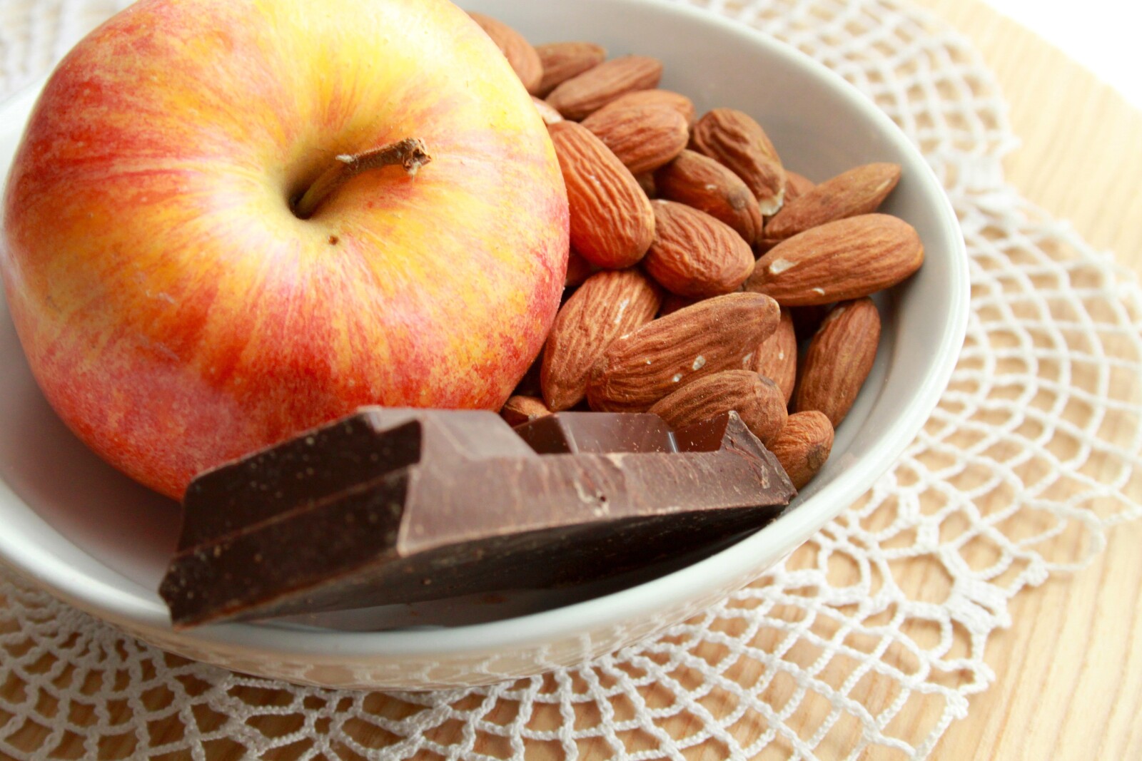 a bowl with an apple, almonds, and chocolate 