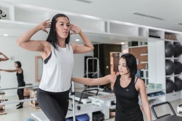 A fitness instructor helping a woman on a pilates machine 