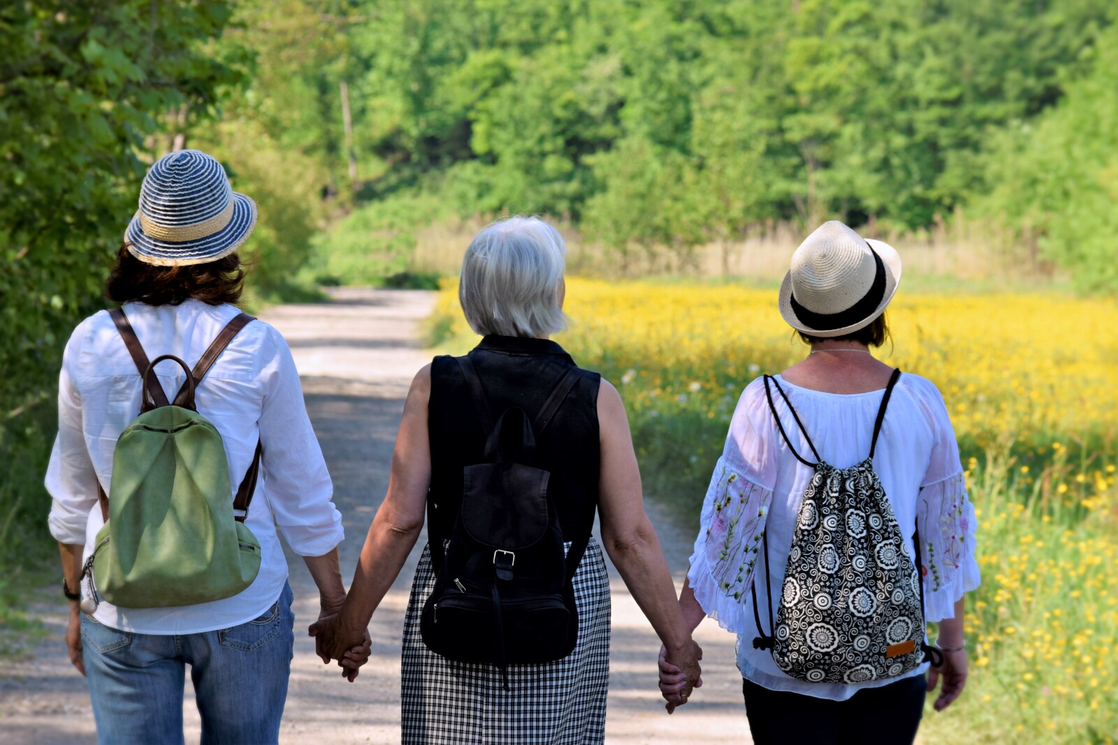 three people holding hands walking on a gravel path