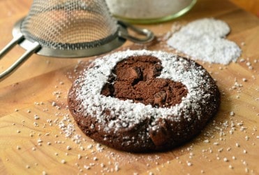 a brown cookie with powdered sugar on top outlining the shape of a heart