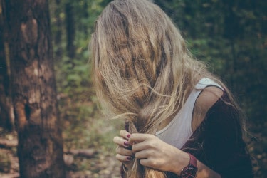 A woman in the woods, braiding her hair with her hair covering her face 