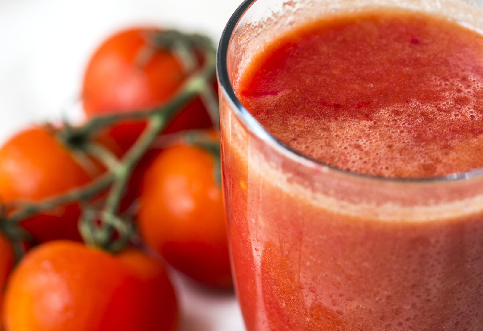 a close photo of a cup of red juice and some blurred tomatoes 