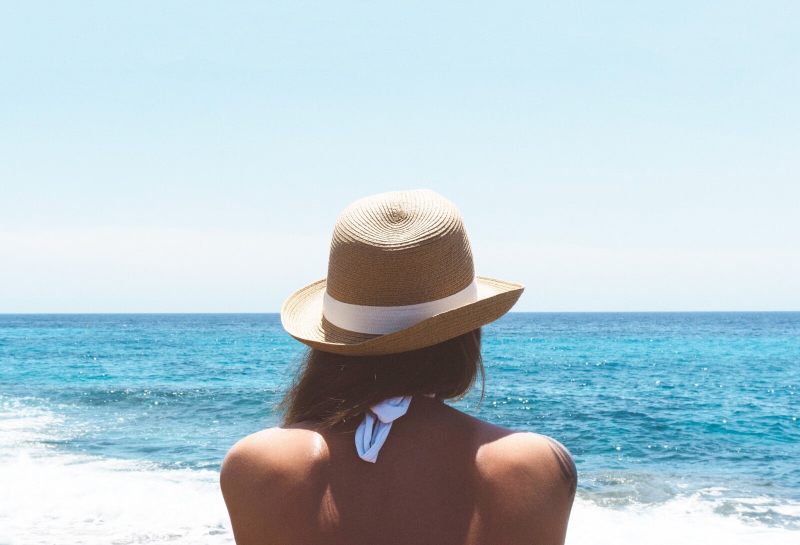the back of a woman facing the ocean in a hat 