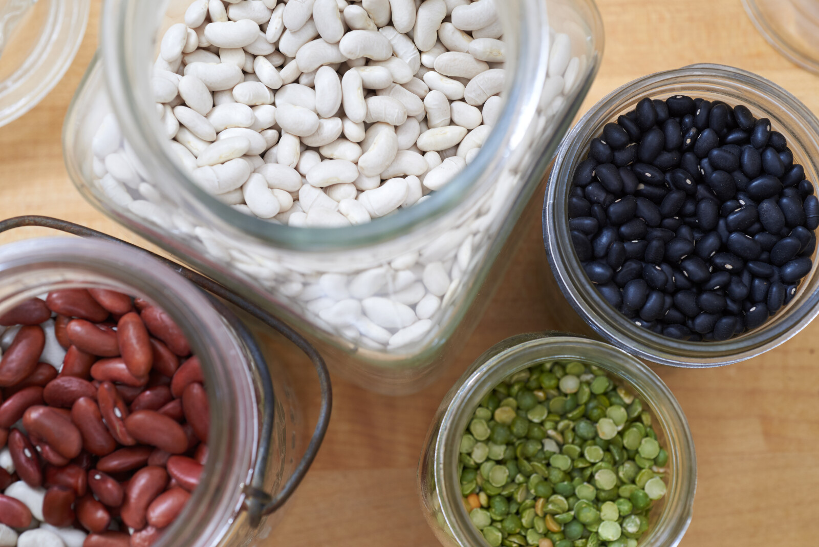 a photo of four different types of beans in jars
