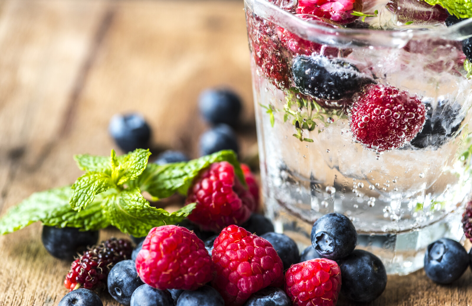 a glass of sparkling water with fruits and berries inside 