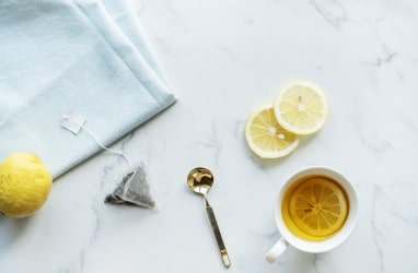 a cup of tea, lemon slices, and a spoon on a white countertop 