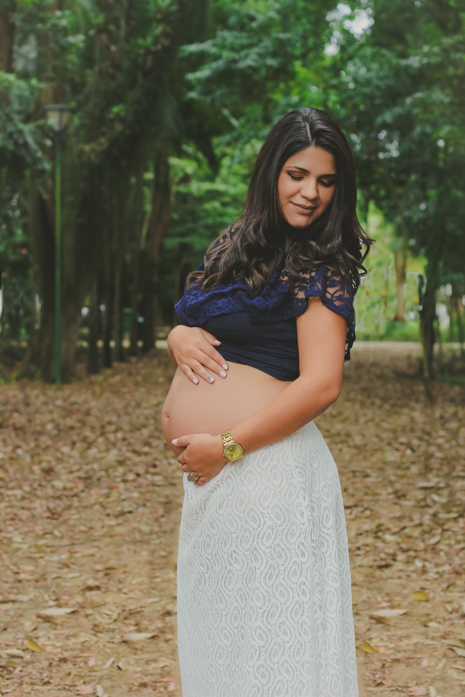 woman in a park holding her pregnant stomach facing the camera 