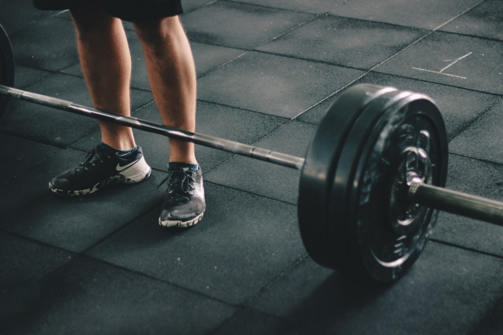 a photo of a barbell with weight on the side on the ground with someone standing behind it