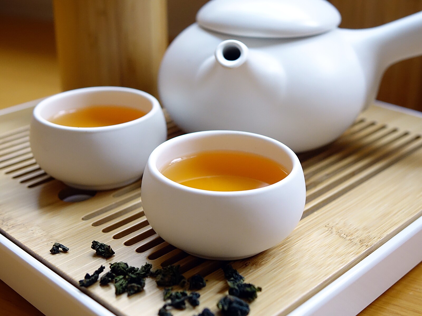 a tea pot and two cups of green tea on a wooden platter 