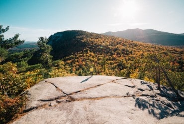 person standing at the top of a mountain looking over some fall foliage 