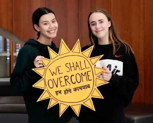 two female students holding a sign saying we shall overcome