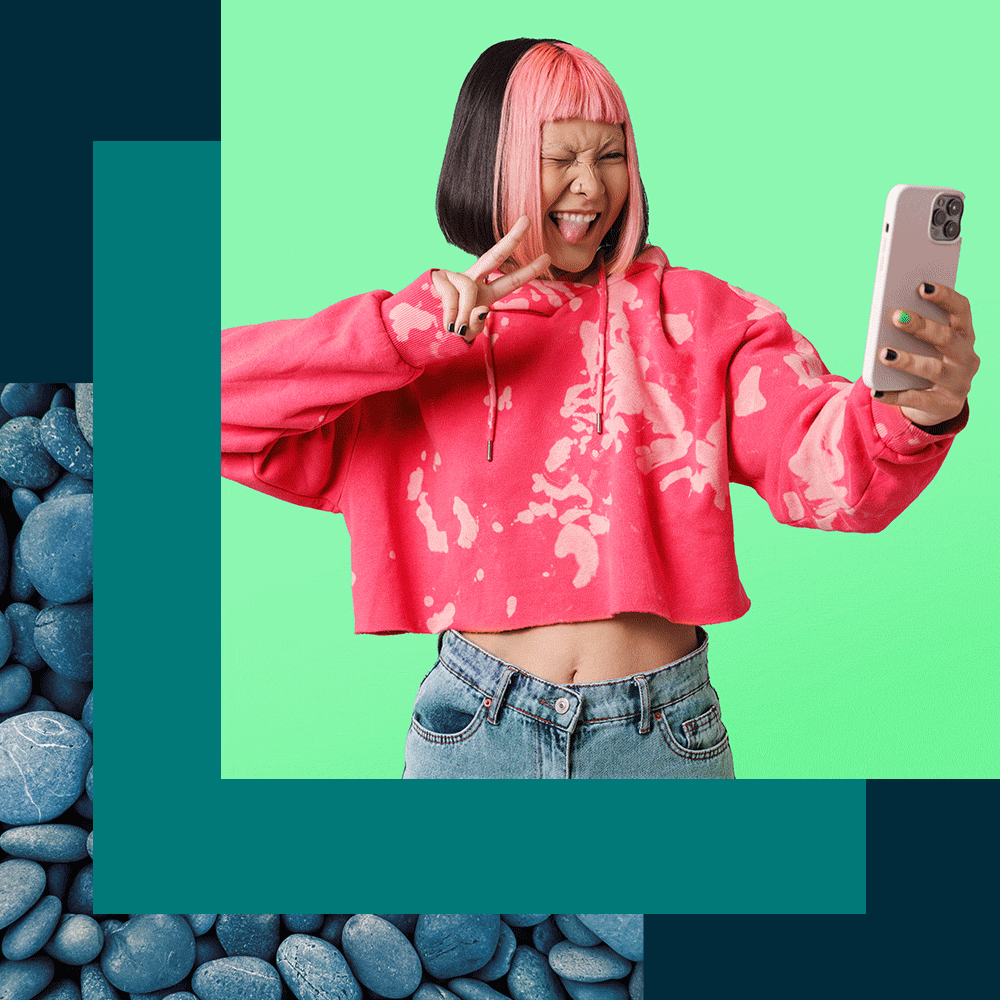 a woman in a pink sweatshirt and pink hair holds a cell phone in her hands.
