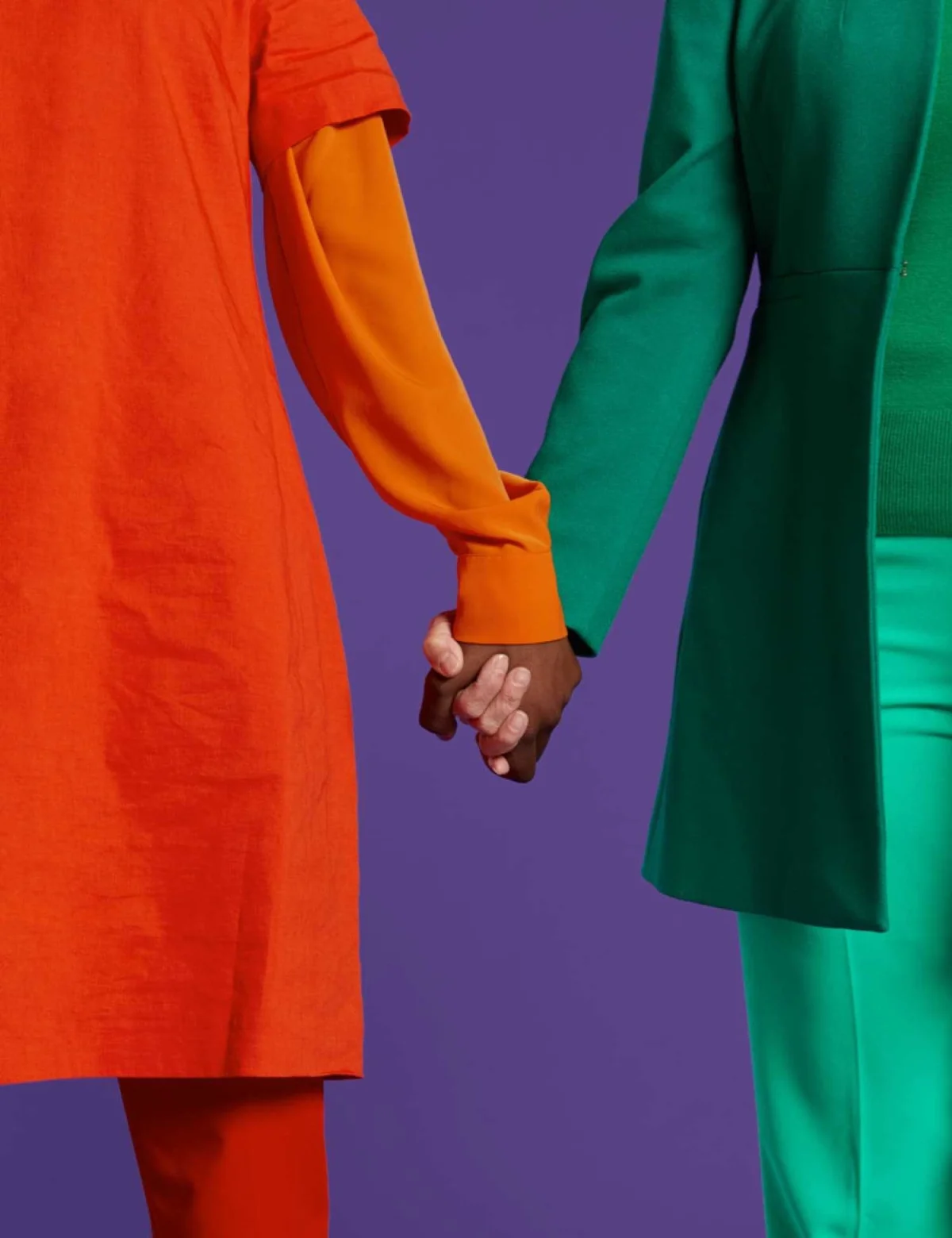 Two people wearing orange and green clothing holding hands in a purple background.