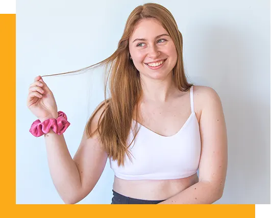 A photo of a girl holding a piece of hair smiling wearing a hair scrunchie on her arm
