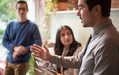 a man in a tie speaks to a group of people in a meeting.