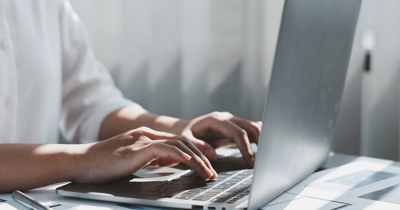 Nahaufnahme eines Laptops, an dem eine Person sitzt und arbeitet in kühlen Grautönen.