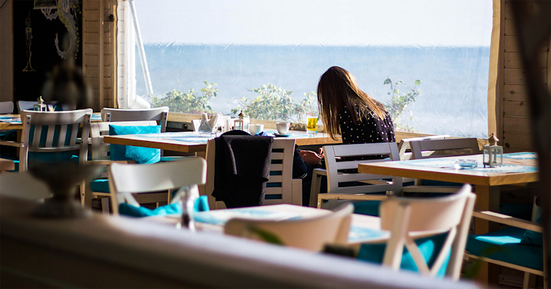 Frau sitzt im Café mit Aussicht aufs Wasser