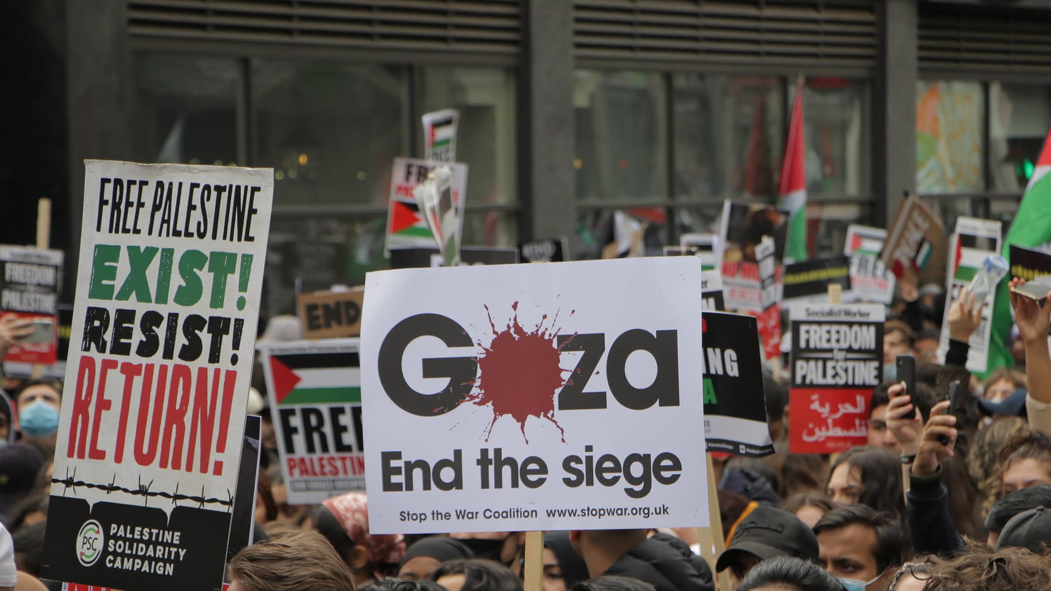 Placards at a protest in solidarity with Palestine. Text reads 'Free Palestine. Exist! Resist! Return!' and 'Gaza. End the siege.'