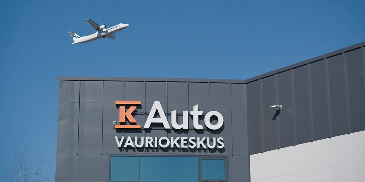 K-Auton Vauriokorjaamon yli lentää lentokone.