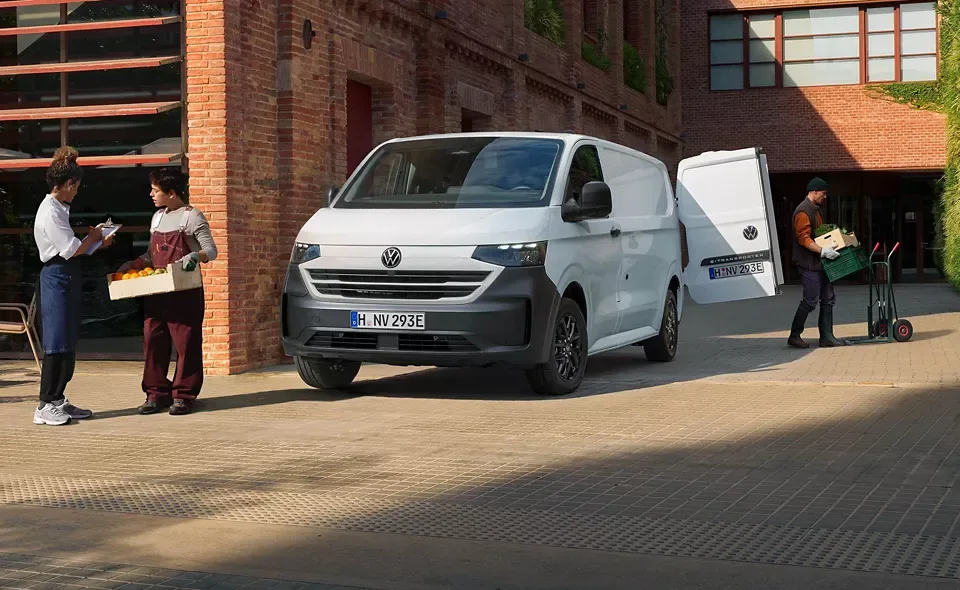 Useita henkilöitä lastaamassa valkoista Volkswagen Transporteria.