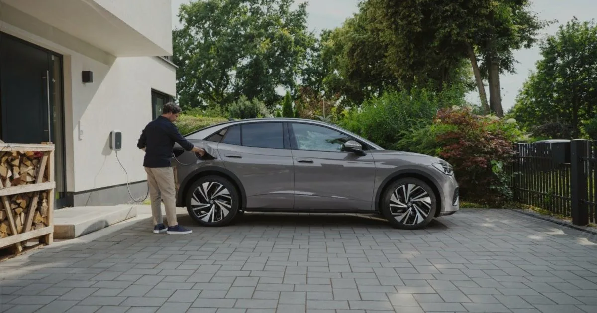 Kuljettaja laittamassa harmaata Volkswagen ID.5 -sähköautoa lataukseen kotilatauslaitteeseen