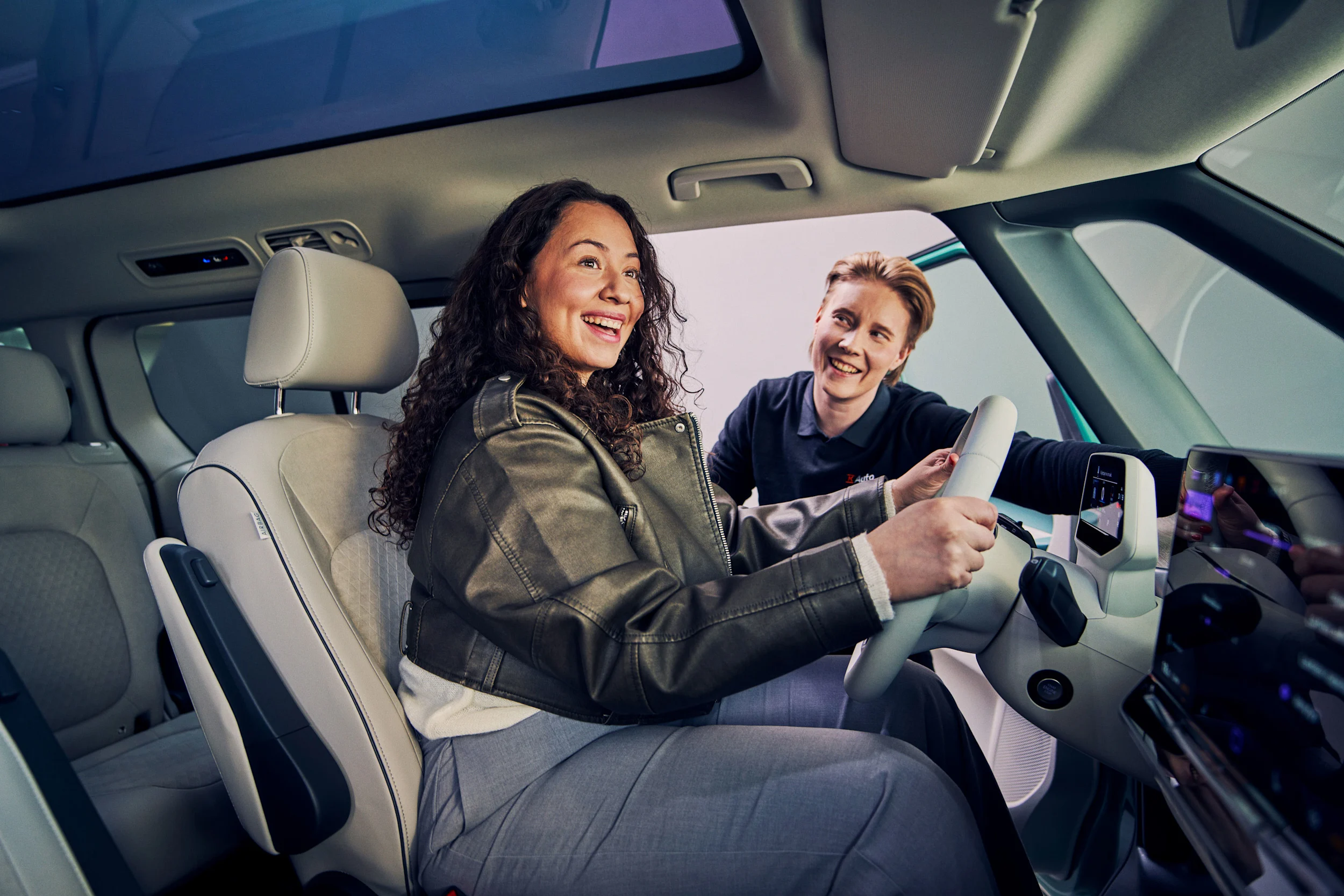 K-Auton myyjä esittelee autoa autossa istuvalle naiselle 