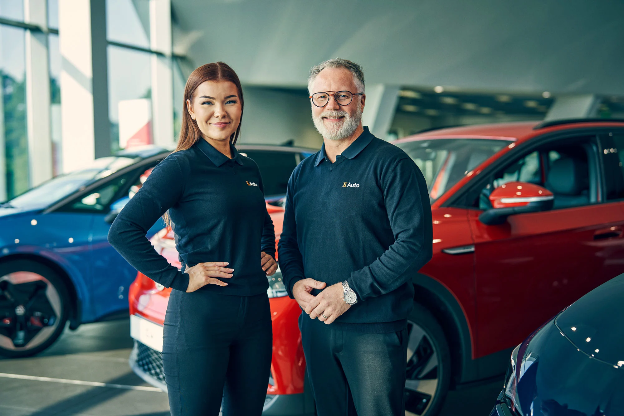 K-Auton kaksi automyyjää sekä autovalikoima heidän takana