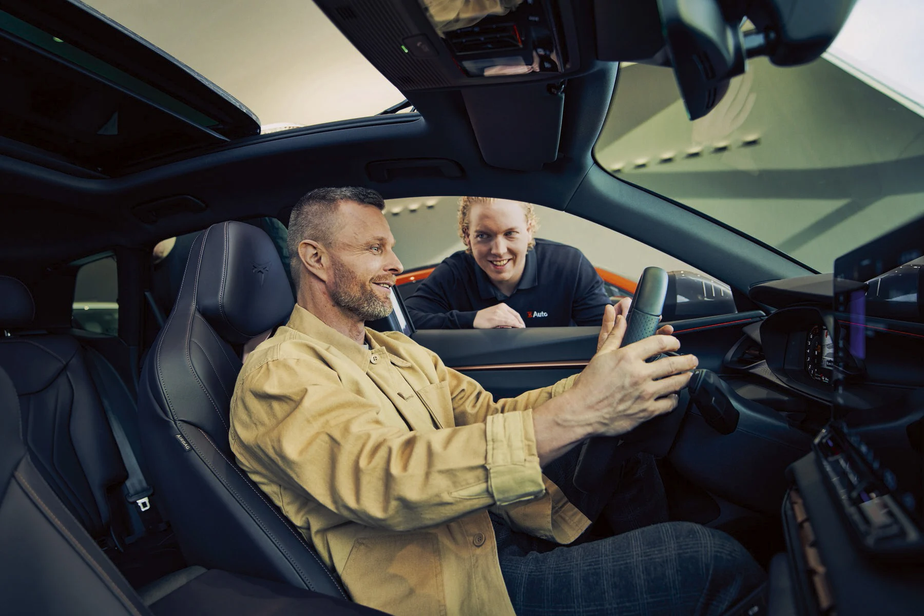 Myyjä esittelee autossa istuvalle asiakkaalle autoa.