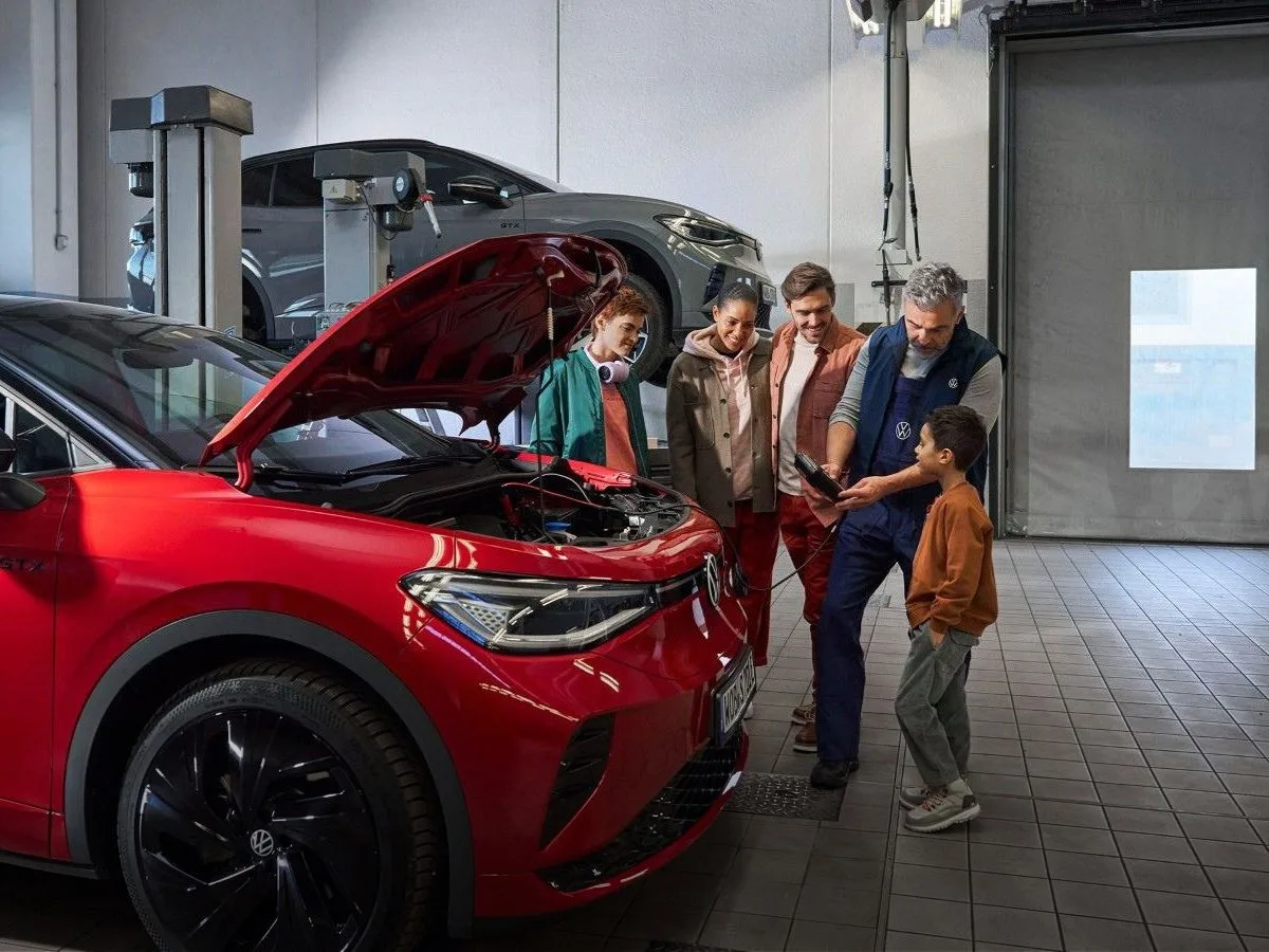 Punainen Volkswagen ID.4 -sähköauto huollossa. Perhe seuraa vierestä automekaanikon työskentelyä.