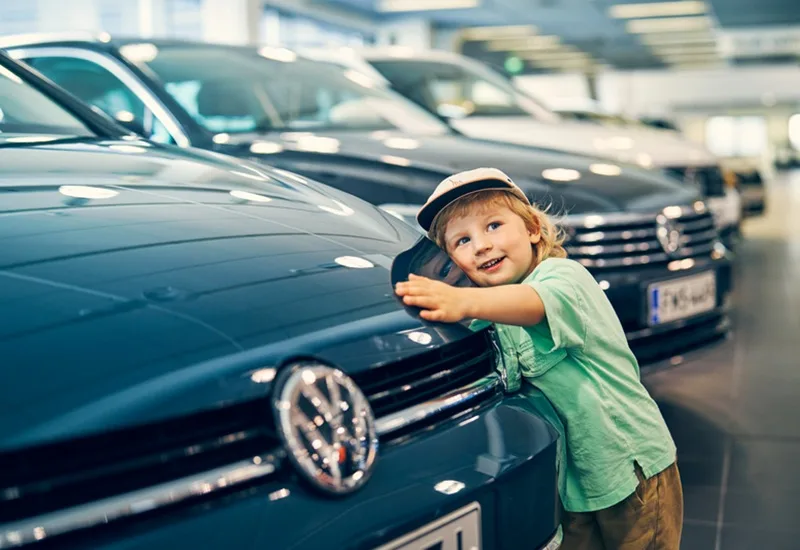 Lapsi halaa sinistä Volkswagenia autohallissa.
