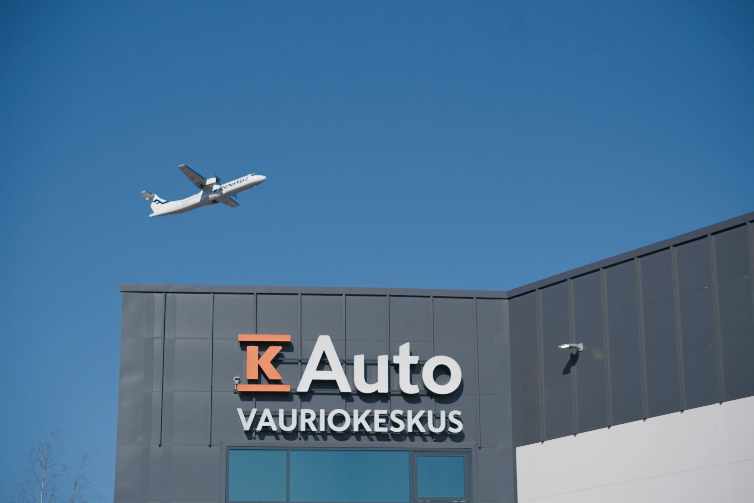 K-Auton Vauriokorjaamon yli lentää lentokone.