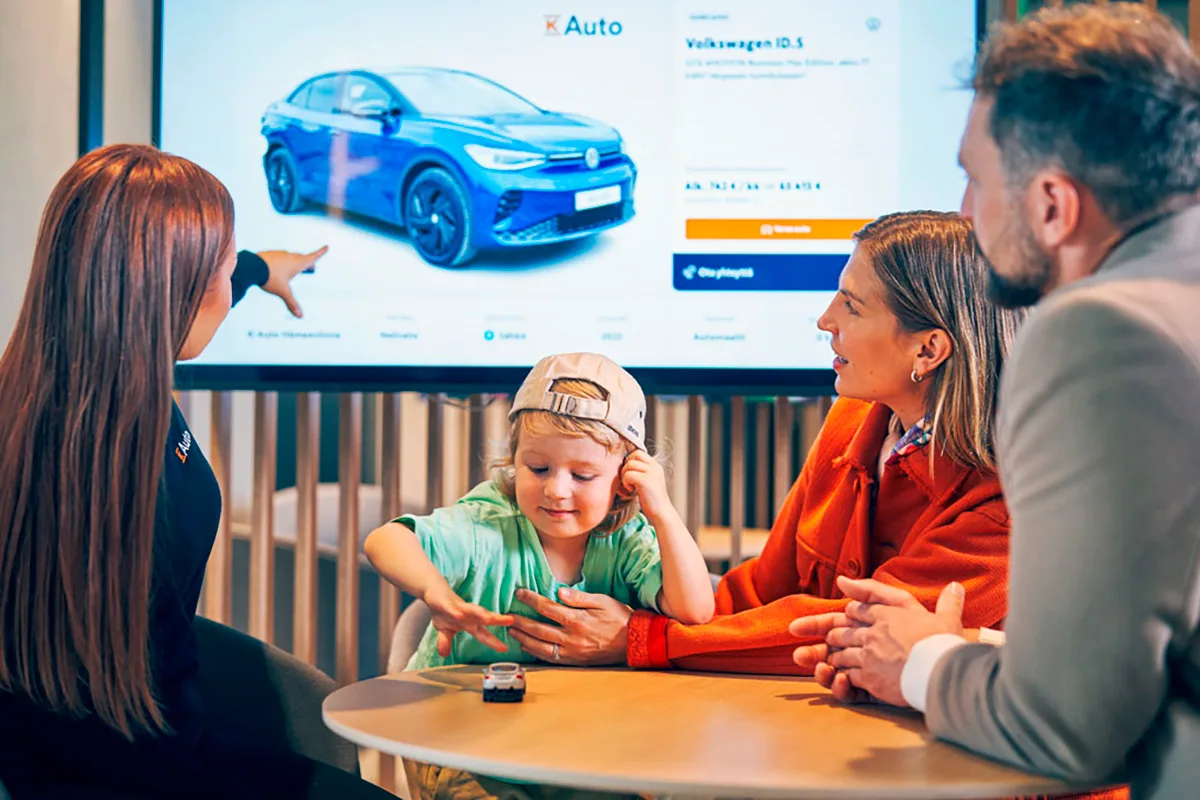 K-Auton myyjä esittelee auton ruudulta perheelle.